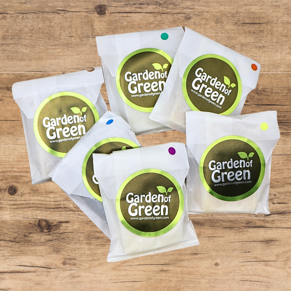 6 -1 oz bars of soap set out in a circle, all wrapped in white packaging with a green garden of green sticker on each one. they are on a light wood background