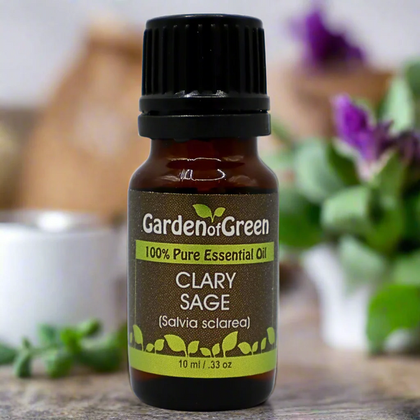 Clary Sage Garden of green essential oil front view sitting on a wood table with a leaf on the lower left hand side. kitchen in the background with a diffuser and a plant