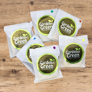 6 -1 oz bars of soap set out in a circle, all wrapped in white packaging with a green garden of green sticker on each one. they are on a light wood background 