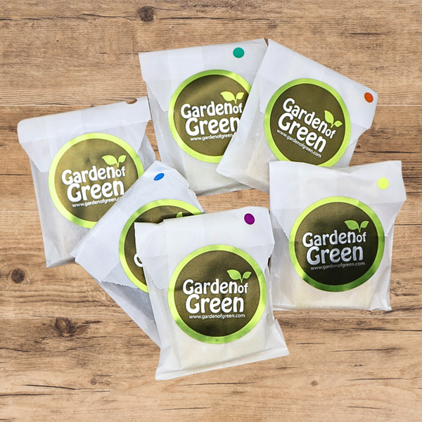 6 -1 oz bars of soap set out in a circle, all wrapped in white packaging with a green garden of green sticker on each one. they are on a light wood background 