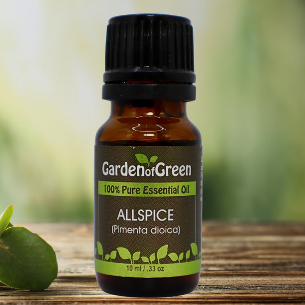 allspice Garden of green essential oil front view sitting on a wood table with a leaf on the lower left hand side. green background with sun shining through the top left.