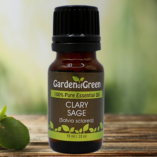 Clary Sage Garden of green essential oil front view sitting on a wood table with a leaf on the lower left hand side. kitchen in the background with a diffuser and a plant