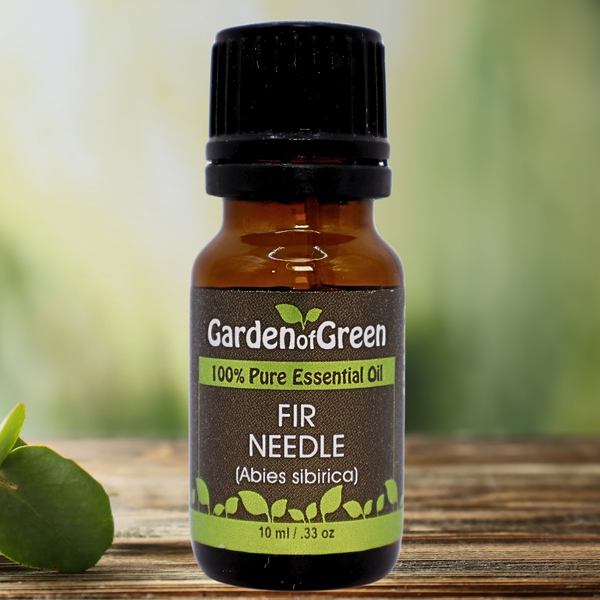 Fir Needle Garden of green essential oil front view sitting on a wood table with a leaf on the lower left hand side. green background with sun shining through the top left.