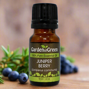 Juniper Berry Garden of green essential oil front view sitting on a wood table with a leaf on the lower left hand side. green background with sun shining through the top left.