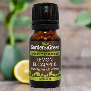 Lemon Eucalyptus Garden of green essential oil front view sitting on a wood table with a leaf on the lower left hand side. green background with sun shining through the top left.
