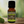 Lime Garden of green essential oil front view sitting on a wood table with a leaf on the lower left hand side. green background with sun shining through the top left.