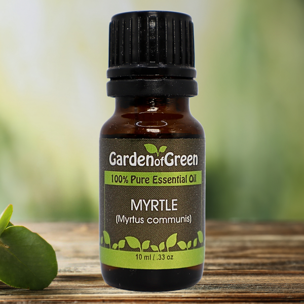 Myrtle Garden of green essential oil front view sitting on a wood table with a leaf on the lower left hand side. green background with sun shining through the top left.