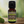 Patchouli Garden of green essential oil front view sitting on a wood table with a leaf on the lower left hand side. green background with sun shining through the top left.