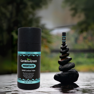 Garden of Green's Solid Lotion Tube front view on the left and a stack of rocks next to it with a small meditate lotion tube sitting on top of the rocks all sitting on water. a forest is in the background