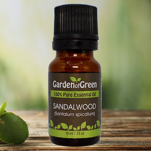 Sandalwood Garden of green essential oil front view sitting on a wood table with a leaf on the lower left hand side. green background with sun shining through the top left.