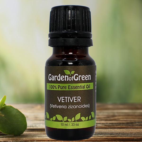 Vetiver Garden of green essential oil front view sitting on a wood table with a leaf on the lower left hand side. green background with sun shining through the top left.