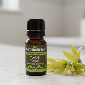 Bottle of Garden of Green Ylang Ylang essential oil on a white surface with yellow flowers.